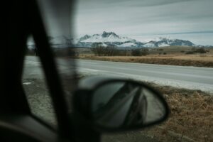 Captivating view of snow-capped mountains through car side mirror on a road trip adventure.
