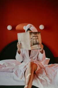Woman in bathrobe reading a magazine on bed in a cozy hotel room.